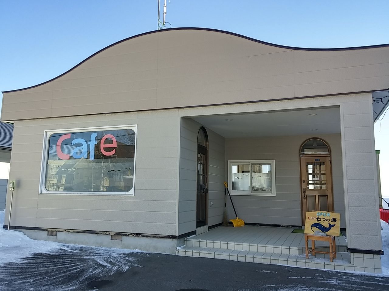 白い外壁に「Cafe」と書かれた窓のあるカフェ七つの海の外観
